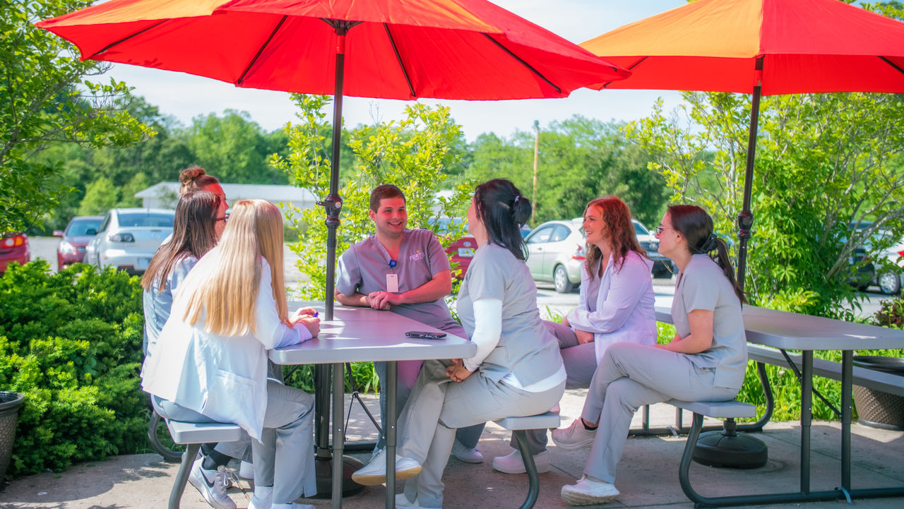 Group of women in scrubs meeting outdoors under umbrellas